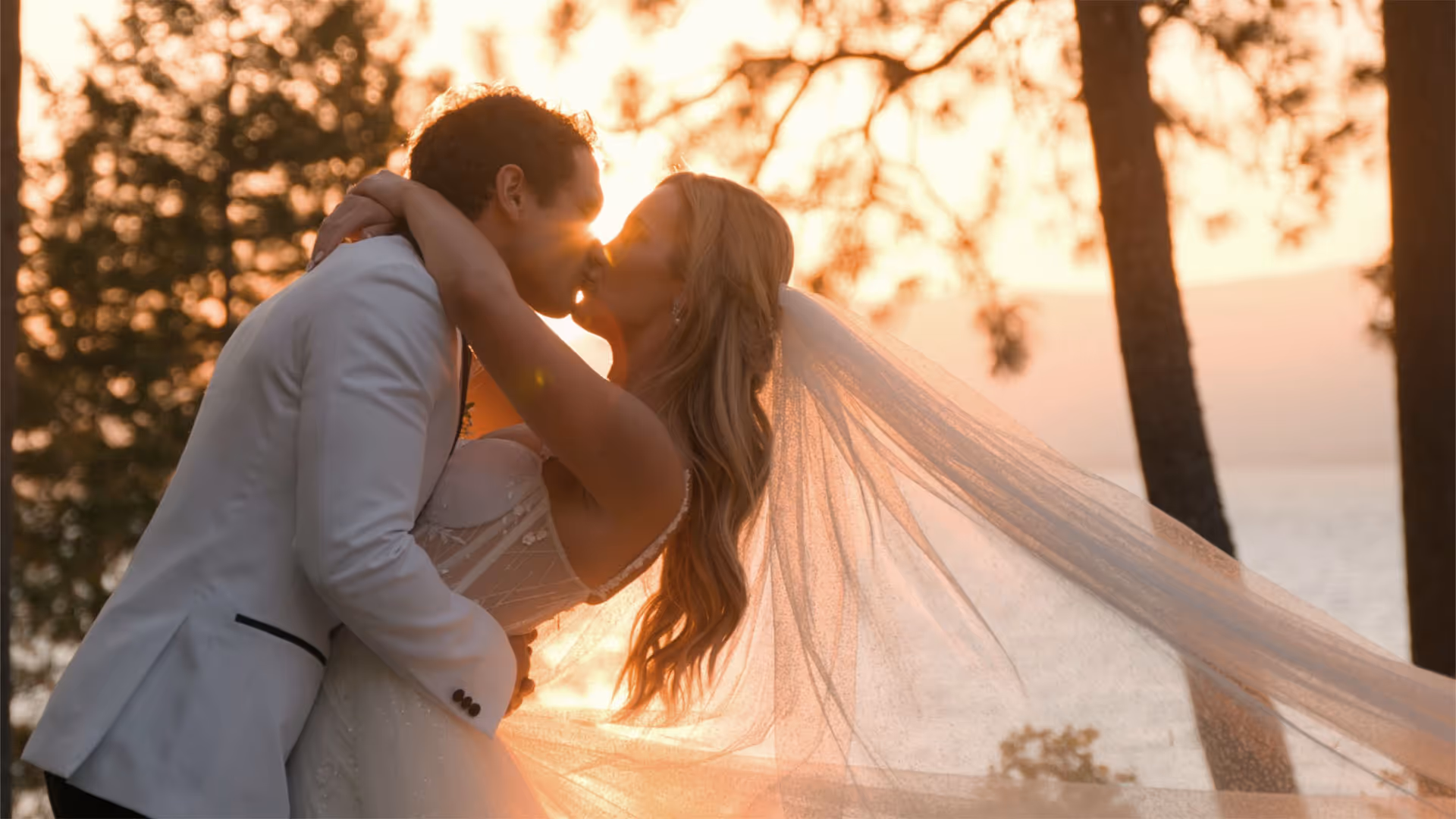 Jenny and Gio kissing at sunset, her veil sweeping out beside them, at their Montana wedding