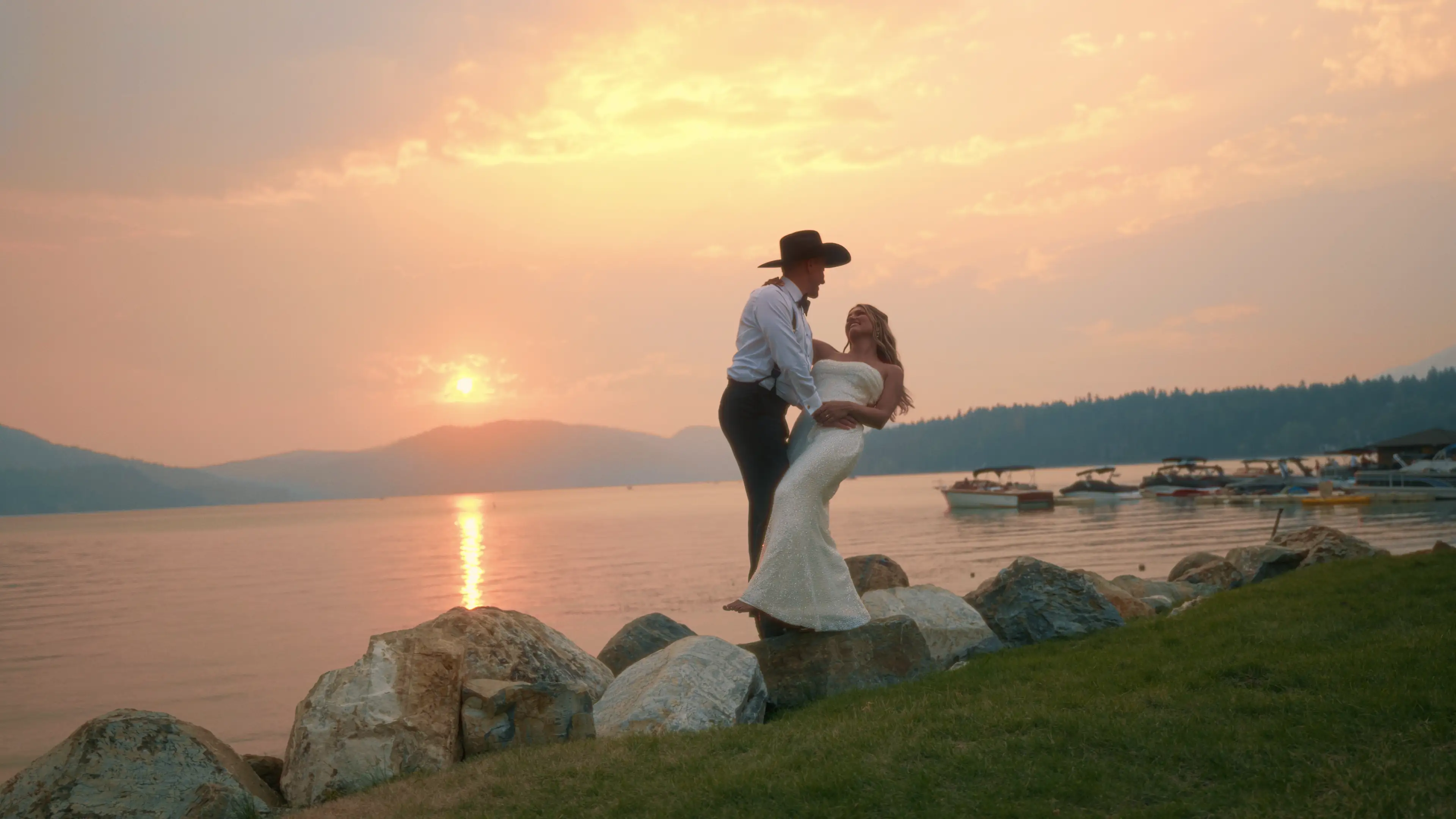 John and Katherine kissing on a rocky Montana lakeshore at sunset in their wedding attire