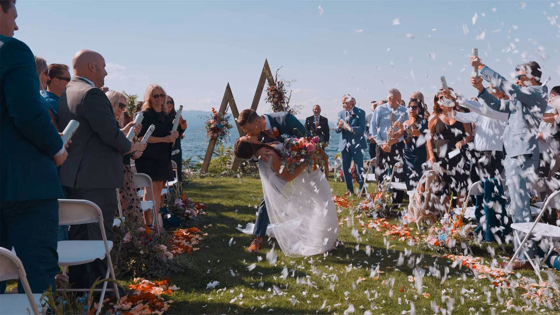 Guests throwing confetti as Nico and Josh kiss at the end of their lakeside Montana wedding ceremony