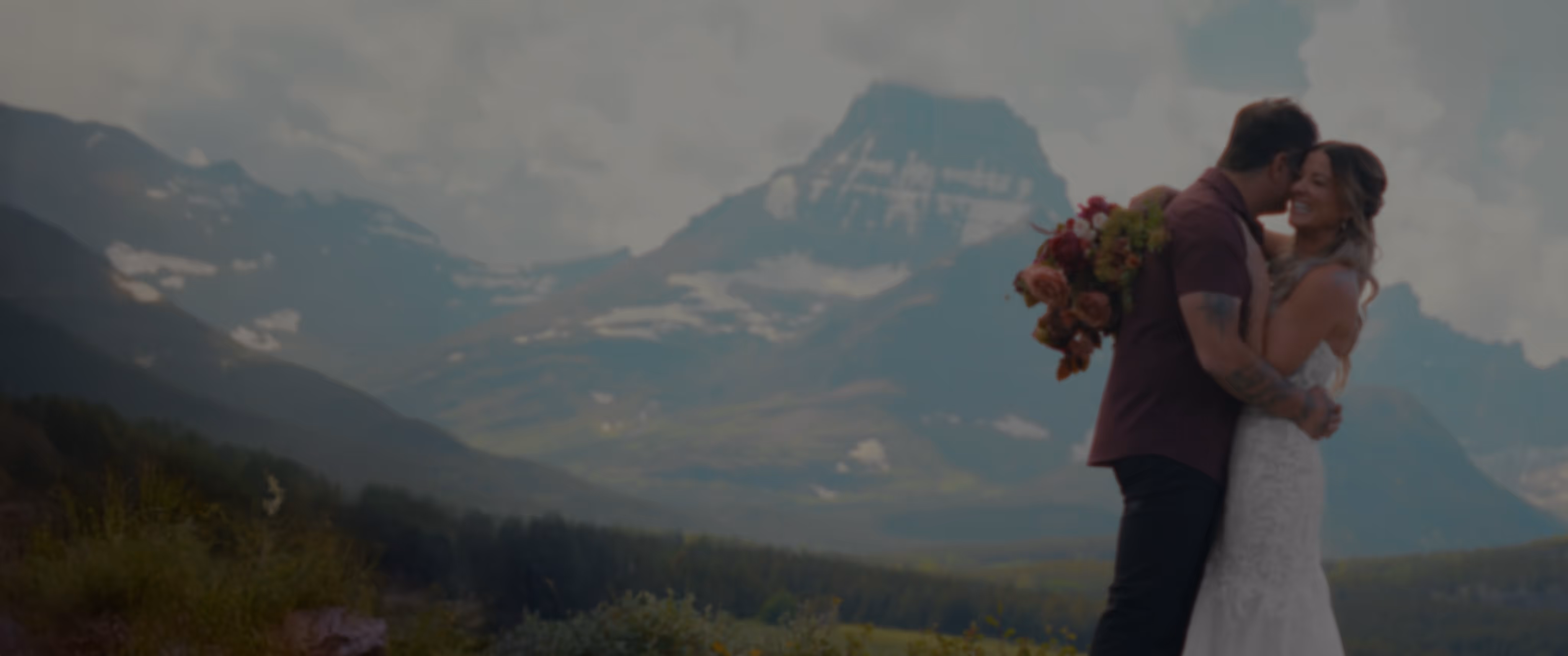 Bride and groom embracing outdoors at a Montana wedding, mountains and partly cloudy sky behind them