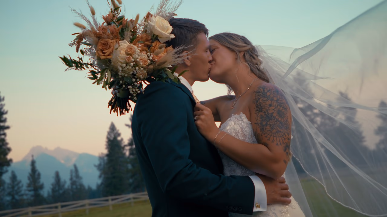 Chloe and Chase kissing at dusk at The Silver Knot in Ronan Montana, her veil lifting in the wind and the Mission Mountains behind them